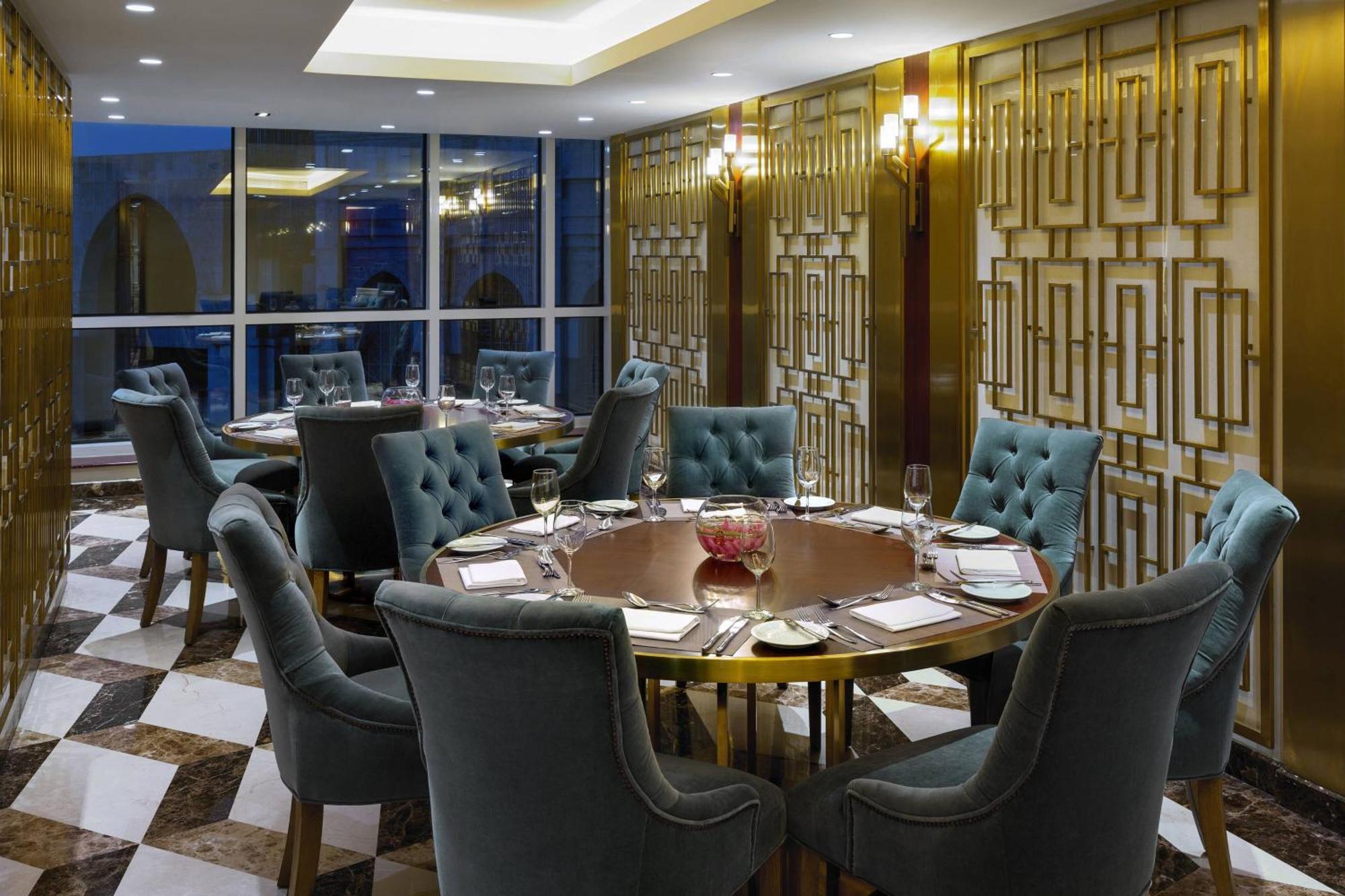 Sheraton Makkah Jabal Al Kaaba Hotel Mekka Exteriér fotografie The photo shows an elegant dining room with a sophisticated ambiance. It features a round wooden table at the center, surrounded by plush chairs upholstered in a soft, teal fabric. The room has a stylish décor, highlighted by a geometrically patterne