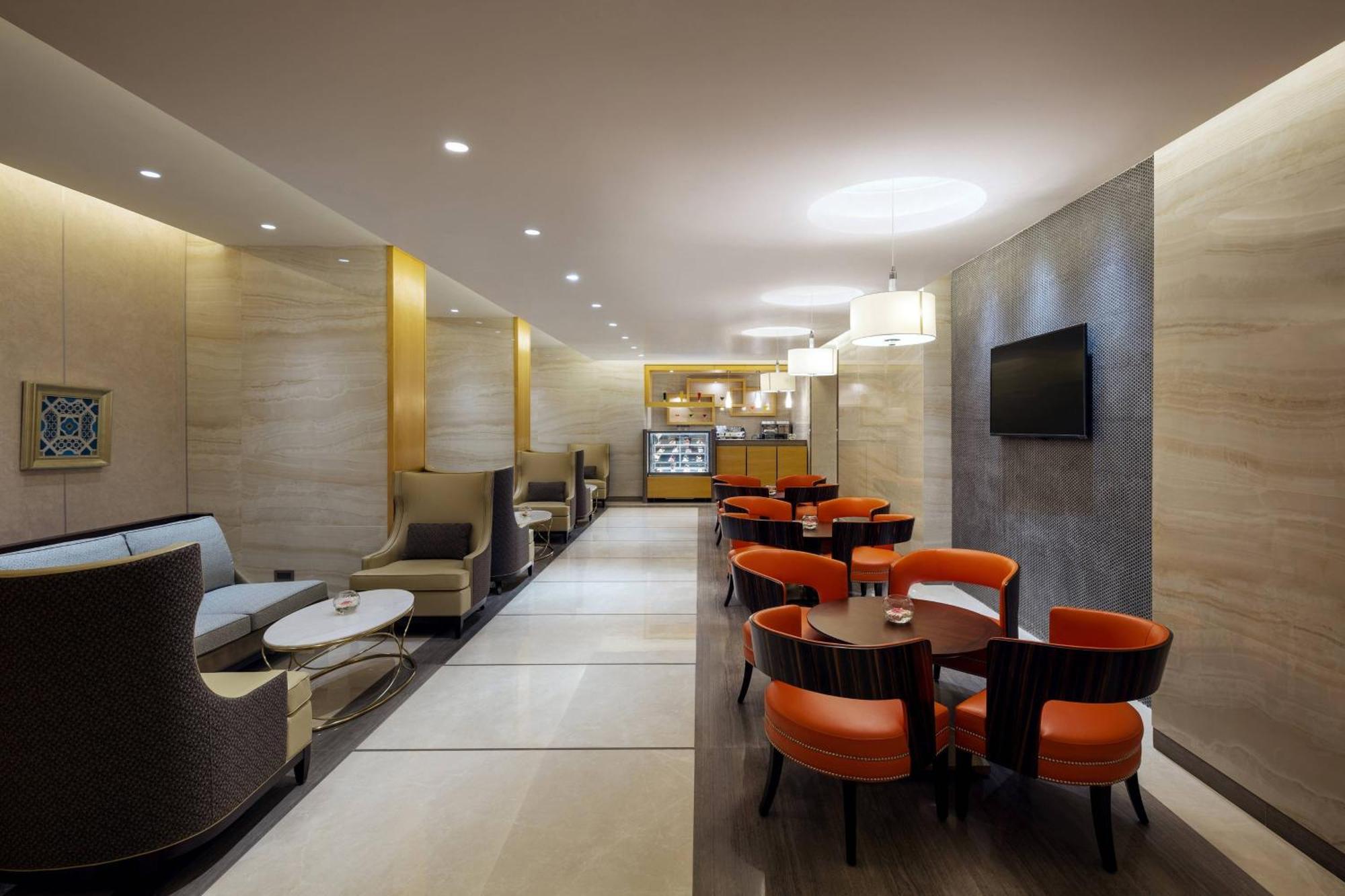 Sheraton Makkah Jabal Al Kaaba Hotel Mekka Exteriér fotografie The photo depicts a modern and elegant lounge or café area. The interior features soft, warm lighting and a combination of neutral and bold color schemes. On the left side, there are comfortable seating arrangements with light-colored sofas and chair